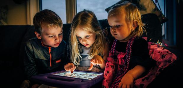 Drie zittende kinderen spelen met een iPad in hun midden.