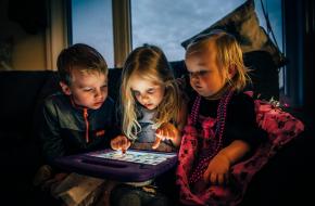 Drie zittende kinderen spelen met een iPad in hun midden.